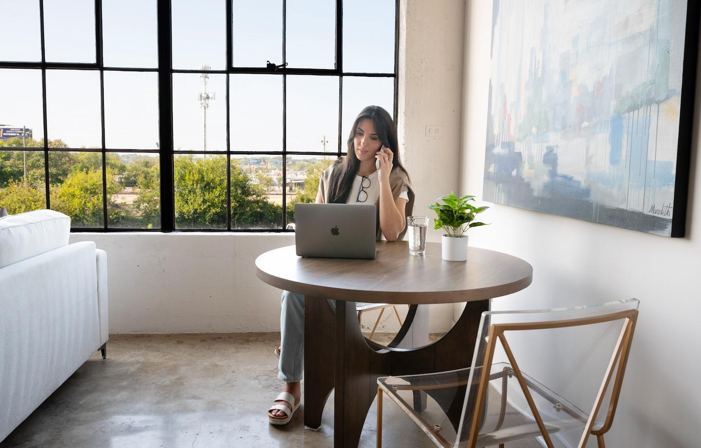 woman on the phone while on laptop at kitchen table